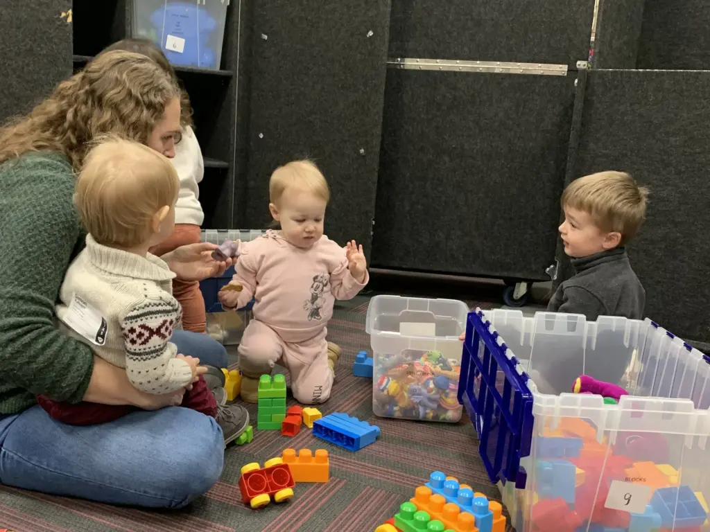 Toddlers and a volunteer playing with colorful blocks in Clarity Kids