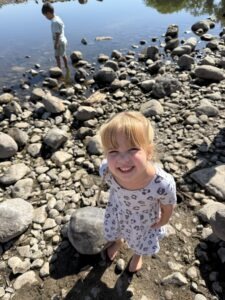 A smiling little girl standing on the rocky shore of a creek