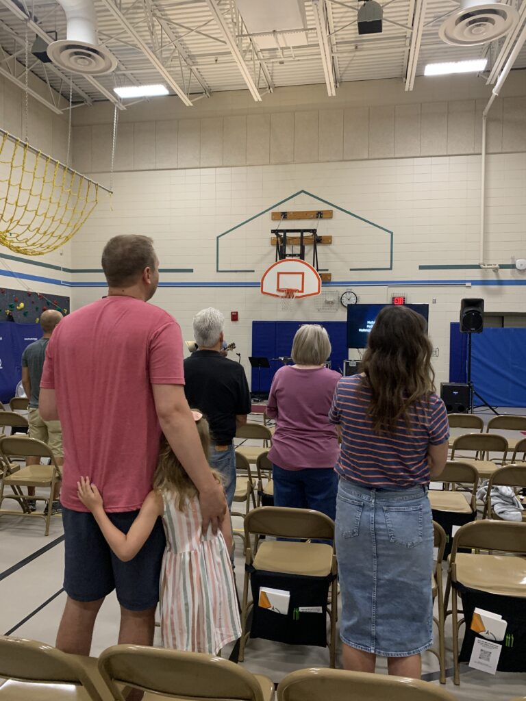 Rows of people standing to sing during Sunday worship in the school gym at Clarity Church