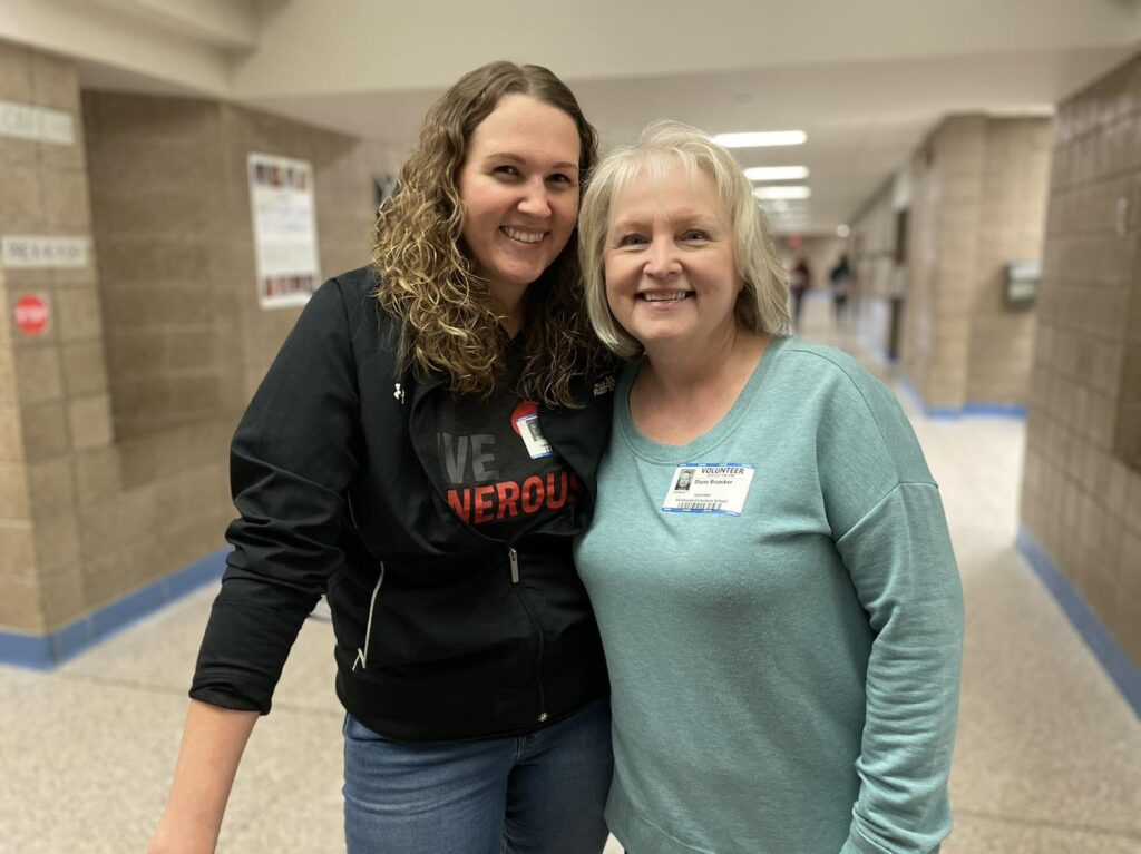 Two volunteers smiling in a school hallway while serving with Every Meal